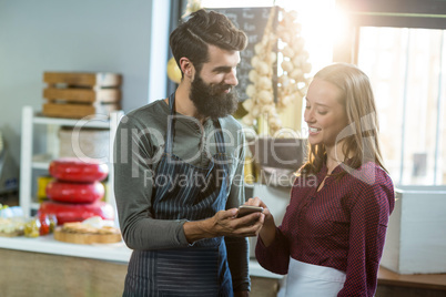 Smiling bakery staff using mobile phone at counter