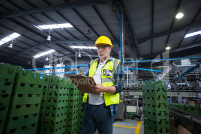 Male factory worker maintaining record on clipboard