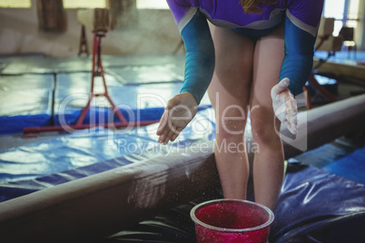 Female gymnast applying chalk powder on her hands before practicing