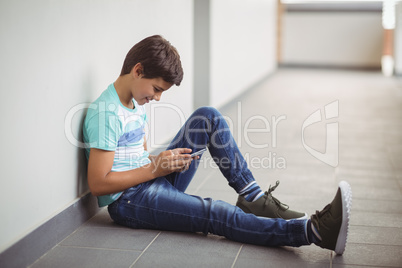 Happy schoolboy using mobile phone in corridor