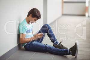 Happy schoolboy using mobile phone in corridor