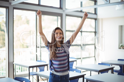 Excited schoolgirl standing with arms up in classroom
