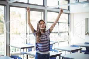 Excited schoolgirl standing with arms up in classroom