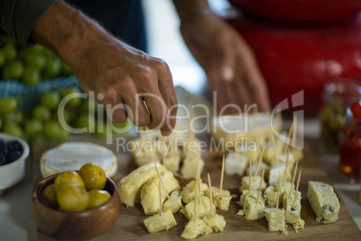 Staff arranging piece of cheese on wooden board in grocery shop