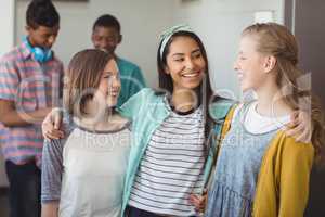 Smiling schoolgirls standing with arms around in corridor