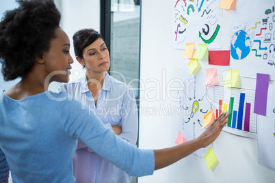 Female graphic designer pointing to the sticky notes on the glass in creative office