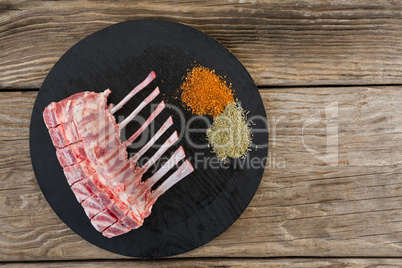 Beef ribs rack and spices on black round tray against wooden background