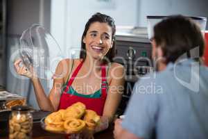 Smiling female staff serving bakery snacks to male customer at counter
