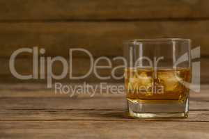 Glass of whisky with ice cube on wooden table