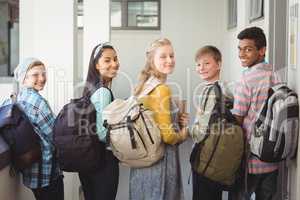 Portrait of smiling students standing with notebook and school bag in corridor