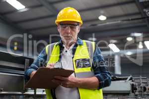 Male factory worker maintaining record on clipboard