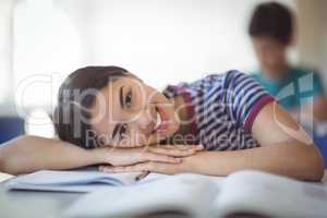 Portrait of happy schoolgirl leaning on bench in classroom