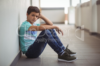 Portrait of sad schoolboy sitting in corridor