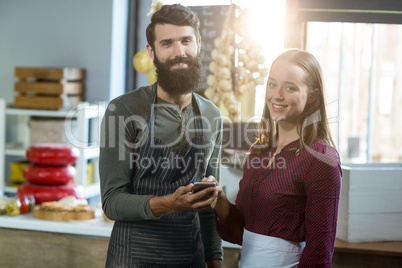 Portrait of smiling bakery staff using mobile phone at counter