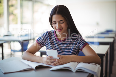 Schoolgirl using mobile phone while studying in classroom
