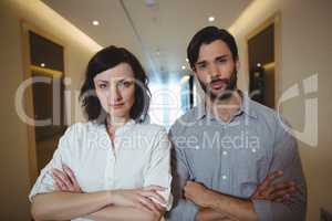 Portrait of male and female executives standing with arms crossed in corridor