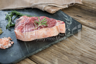 Sirloin chop, rosemary herb and salt on slate board against wooden background