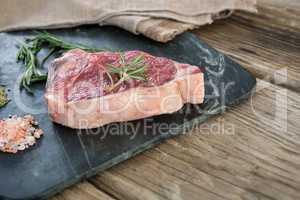 Sirloin chop, rosemary herb and salt on slate board against wooden background