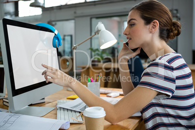 Graphic designer using computer while talking on mobile phone