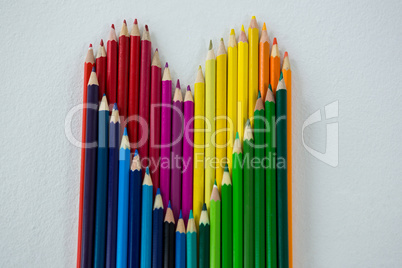 Colored pencils arranged in heart shape on white background