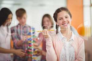 Portrait of smiling schoolgirl holding pencil in classroom