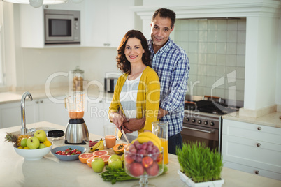 Happy couple embracing while preparing smoothie in kitchen