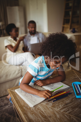 Daughter drawing on book while parents using laptop in background
