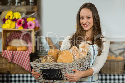 Portrait of smiling female staff holding a basket of baguettes at counter