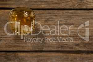 Glass of whisky with ice cube on wooden table