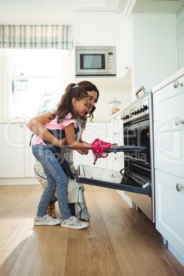 Mother and daughter placing tray of cookies in oven