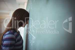 Tired schoolgirl standing with closed eyes near chalkboard in classroom