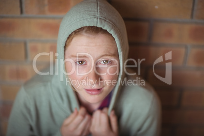 Portrait of sad schoolgirl sitting alone against brick wall