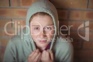 Portrait of sad schoolgirl sitting alone against brick wall