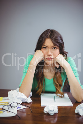 Frustrated female business executive sitting with crumpled papers balls
