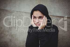 Anxious teenage girl in black hooded jacket standing with hand on face