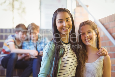 Portrait of smiling schoolgirls standing with arm around in corridor