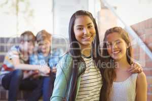 Portrait of smiling schoolgirls standing with arm around in corridor