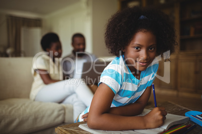 Daughter drawing on book while parents using laptop in background