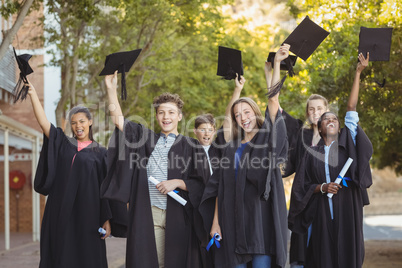 Graduate school kids standing with degree scroll and mortarboard in campus