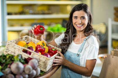 Smiling woman picking bell pepper from the basket from grocery store
