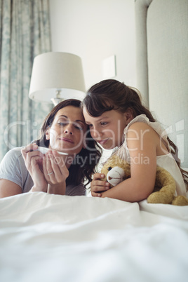 Mother showing temperature on thermometer to her daughter