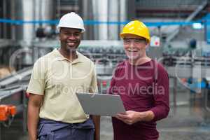 Two factory workers with laptop smiling in the drinks production plant