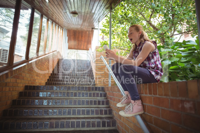 Schoolgirl sitting on brick wall and using mobile phone