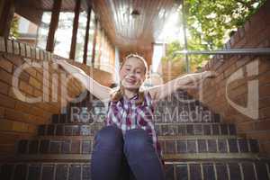 Portrait of happy schoolgirl sitting with arms outstretched on staircase