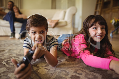 Siblings lying on rug and playing video game