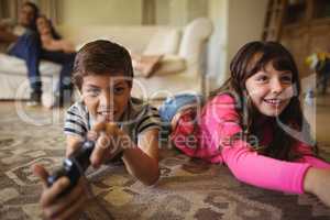 Siblings lying on rug and playing video game