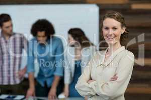 Smiling female business executive standing with arms crossed in office