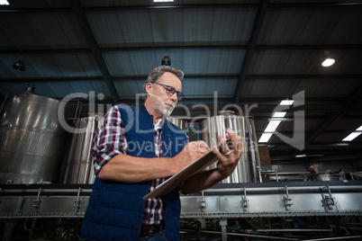 Factory worker writing on clipboard in factory