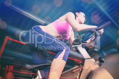 Composite image of determined young woman working out at spinning class