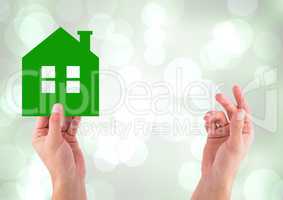 Composite image of Hands holding green home icon against bright background